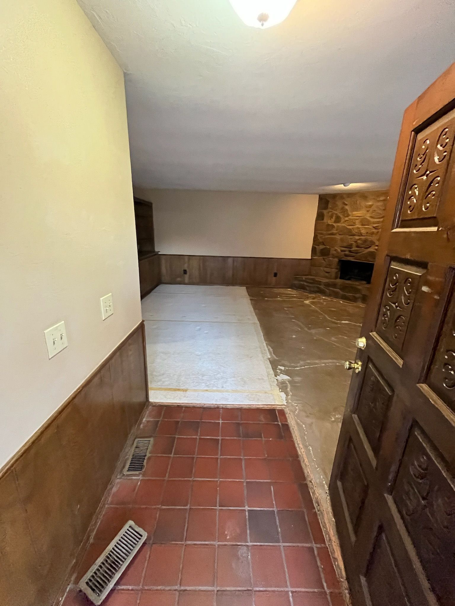 Open doorway to a basement with brick floor, carpet, fireplace, and decorative wooden door.