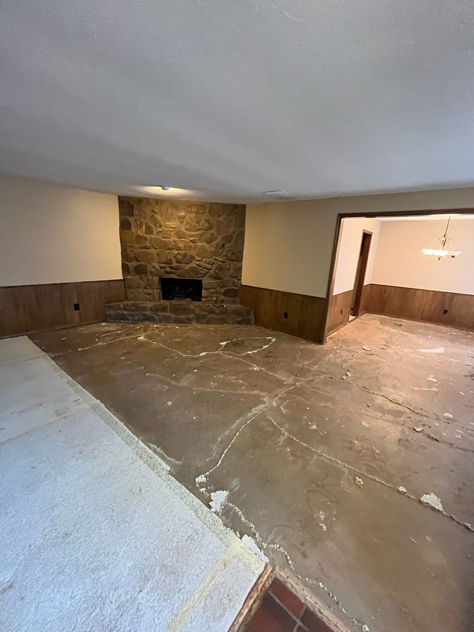Empty room with stone fireplace, beige walls, and damaged concrete floor.