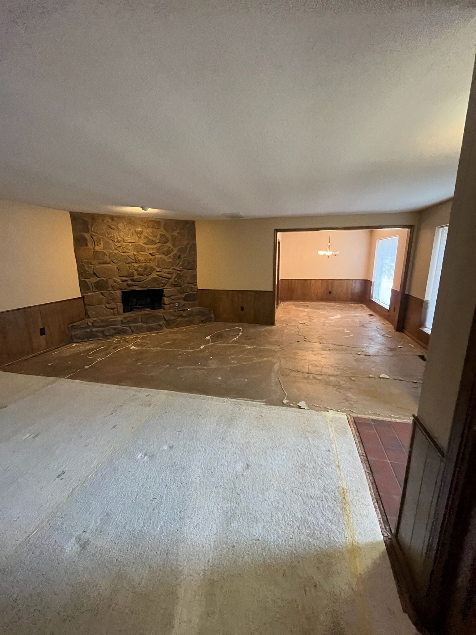 Interior of a room with exposed flooring, a stone fireplace, and an open doorway.