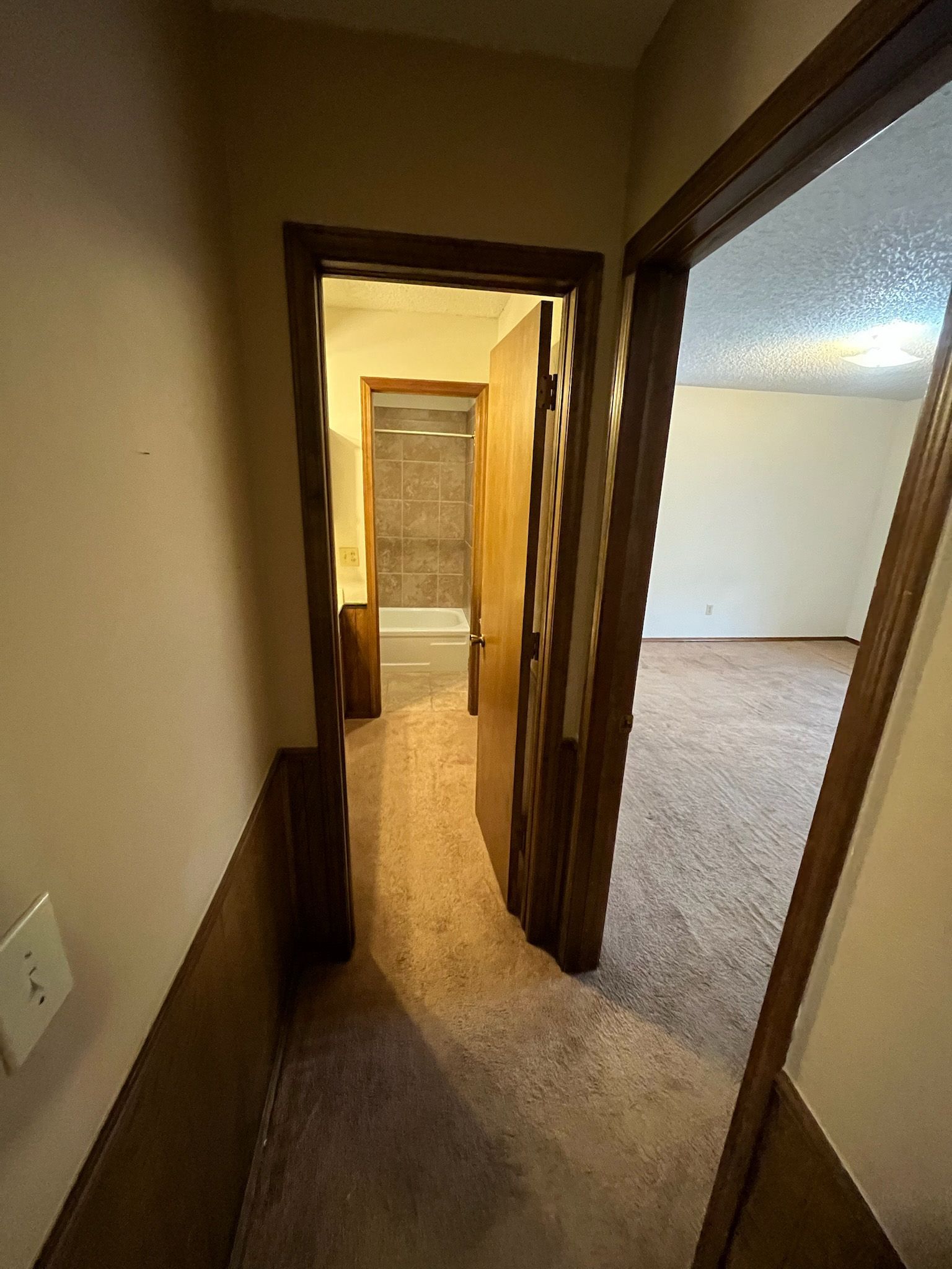 Hallway with doors to rooms. Beige walls, carpet, and trim. One door is open.
