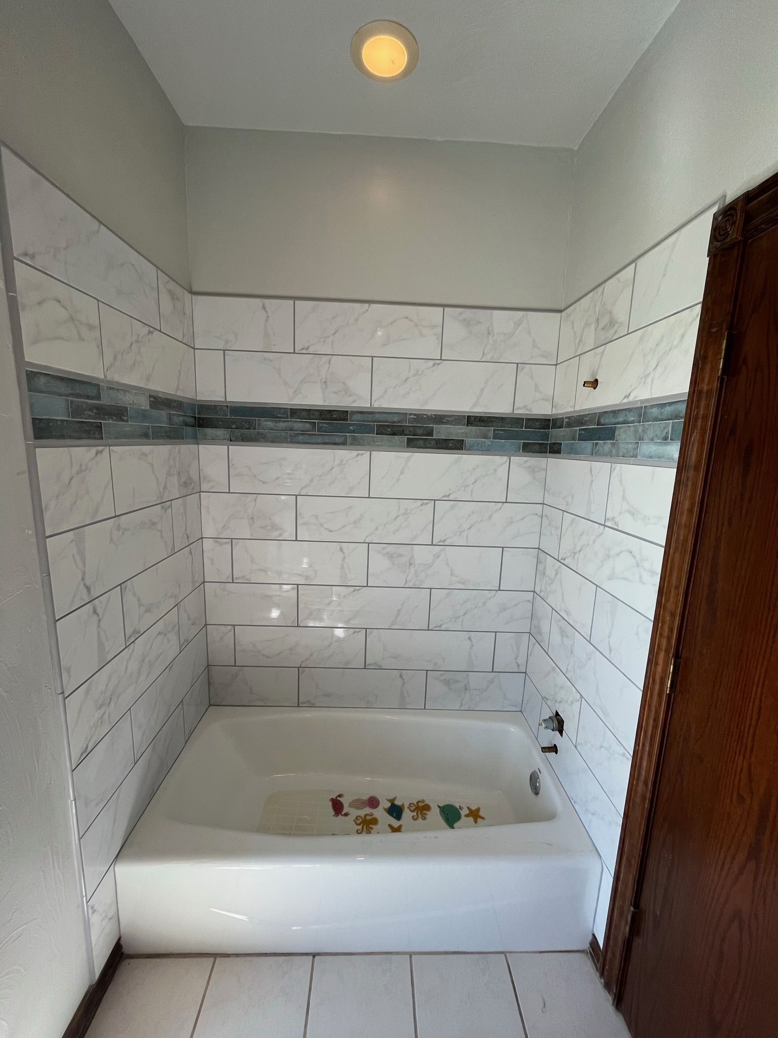 Bathroom with white tile, blue accent tiles, a white bathtub, and a brown door.