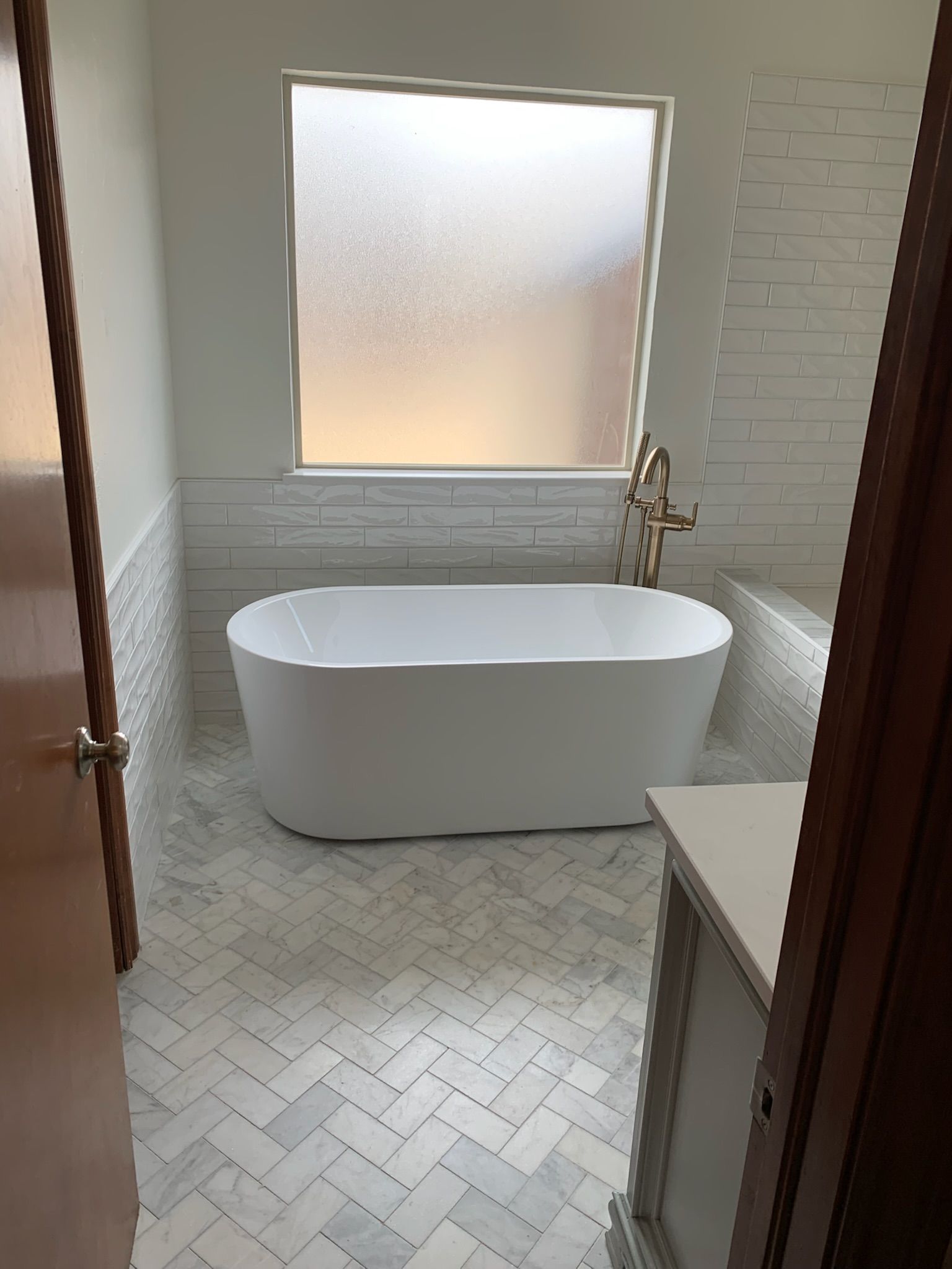 Bathroom with white oval tub, herringbone floor tiles, and frosted window.