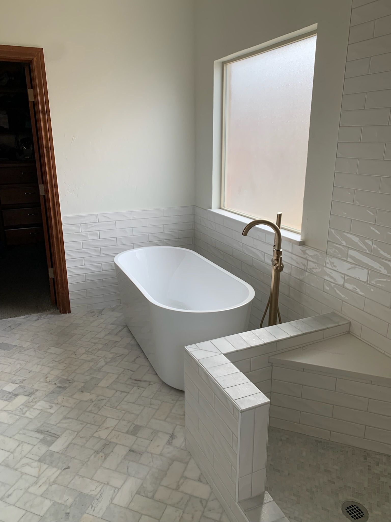 Modern bathroom with a white freestanding tub, gold faucet, and textured white tile.