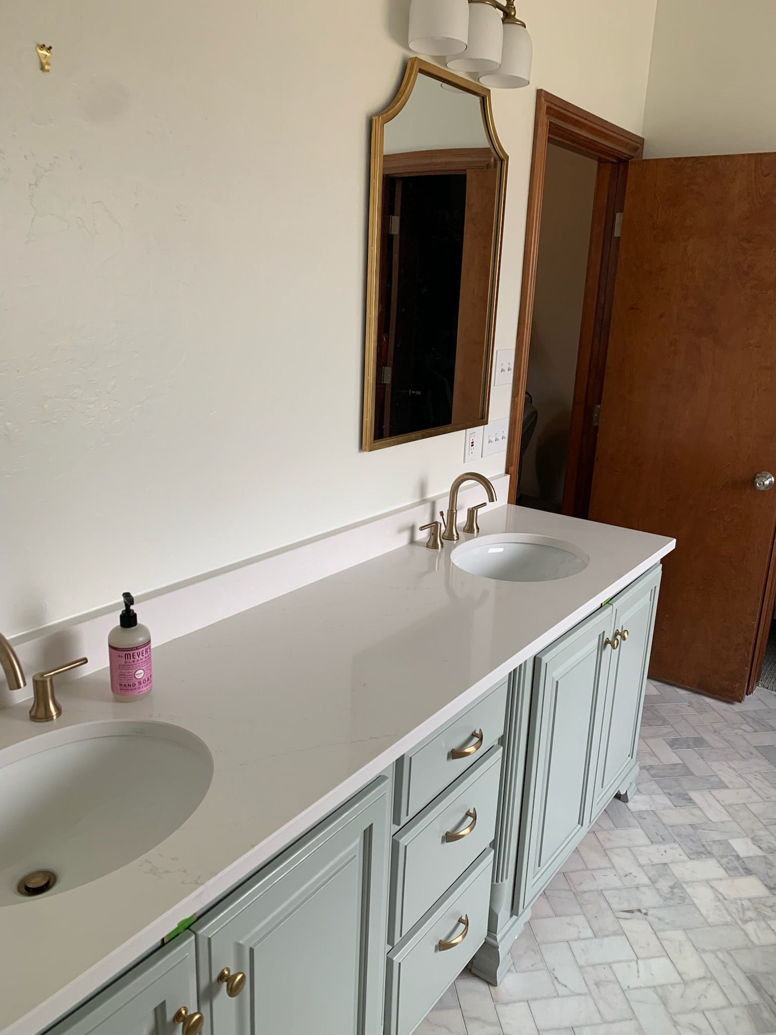 Bathroom with light-blue vanity, white countertop, two sinks, gold fixtures, and gold-framed mirror.