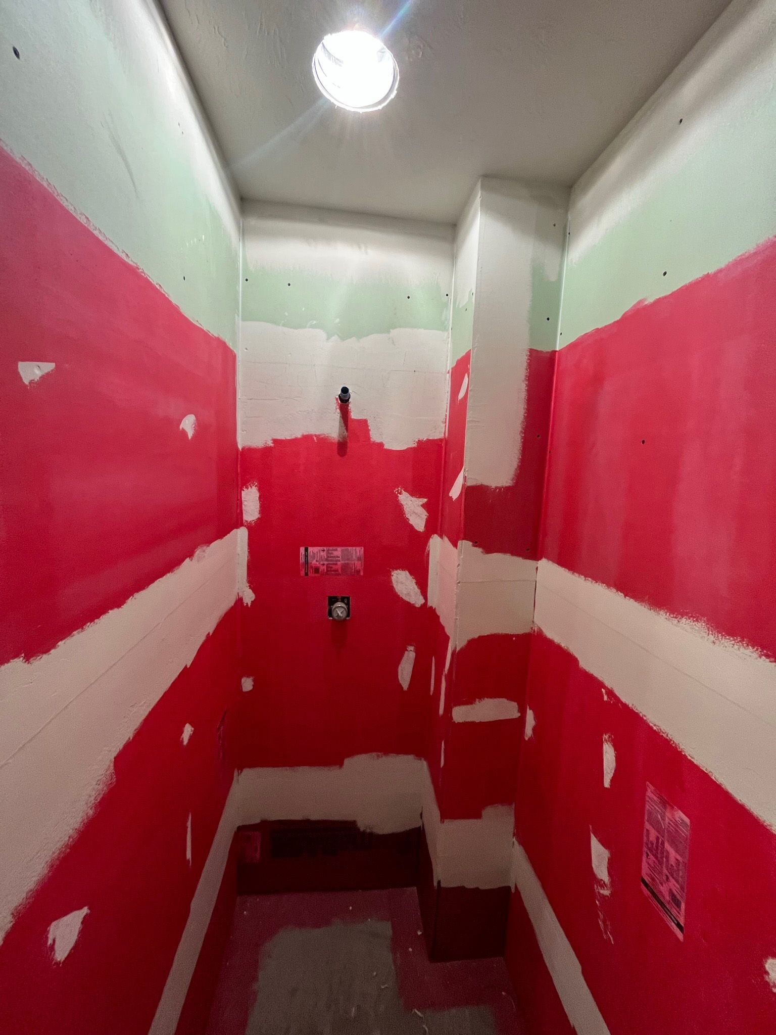 Red and white waterproofed shower walls in a bathroom under construction.