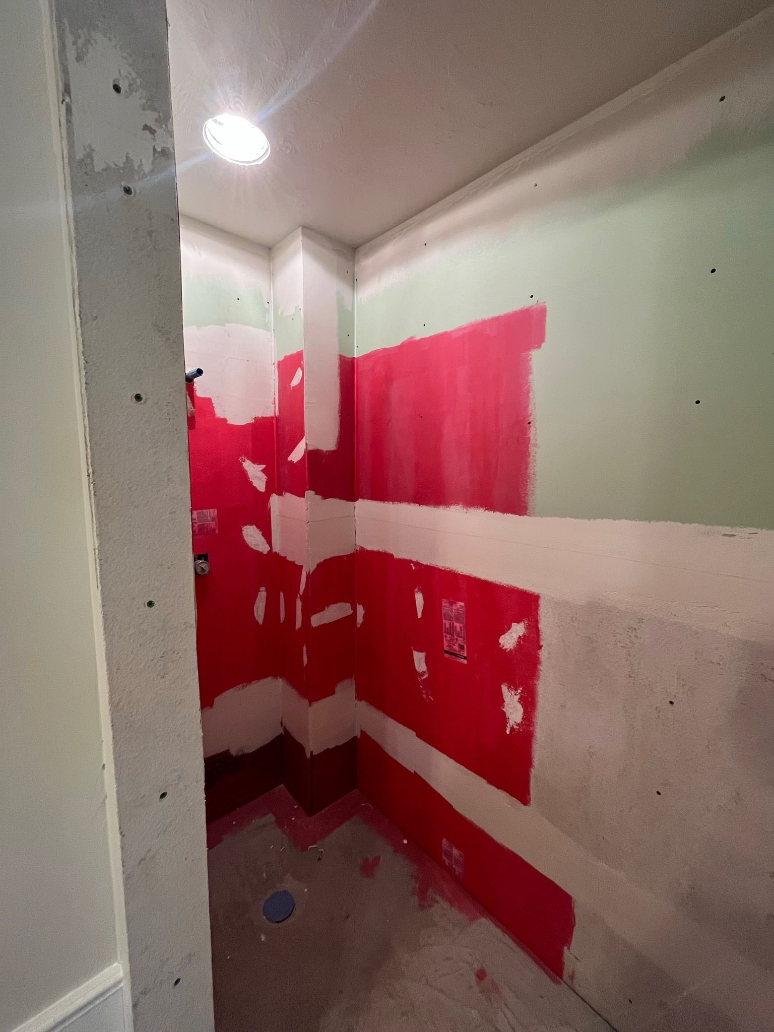 Small bathroom under construction. Red waterproofing paint on walls, white gaps, green walls.