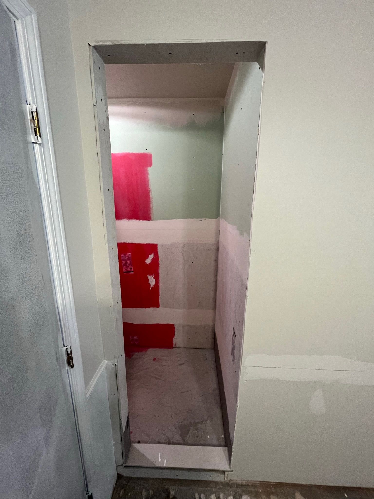 A doorway with exposed drywall leads to a small room. The walls are painted red and green.