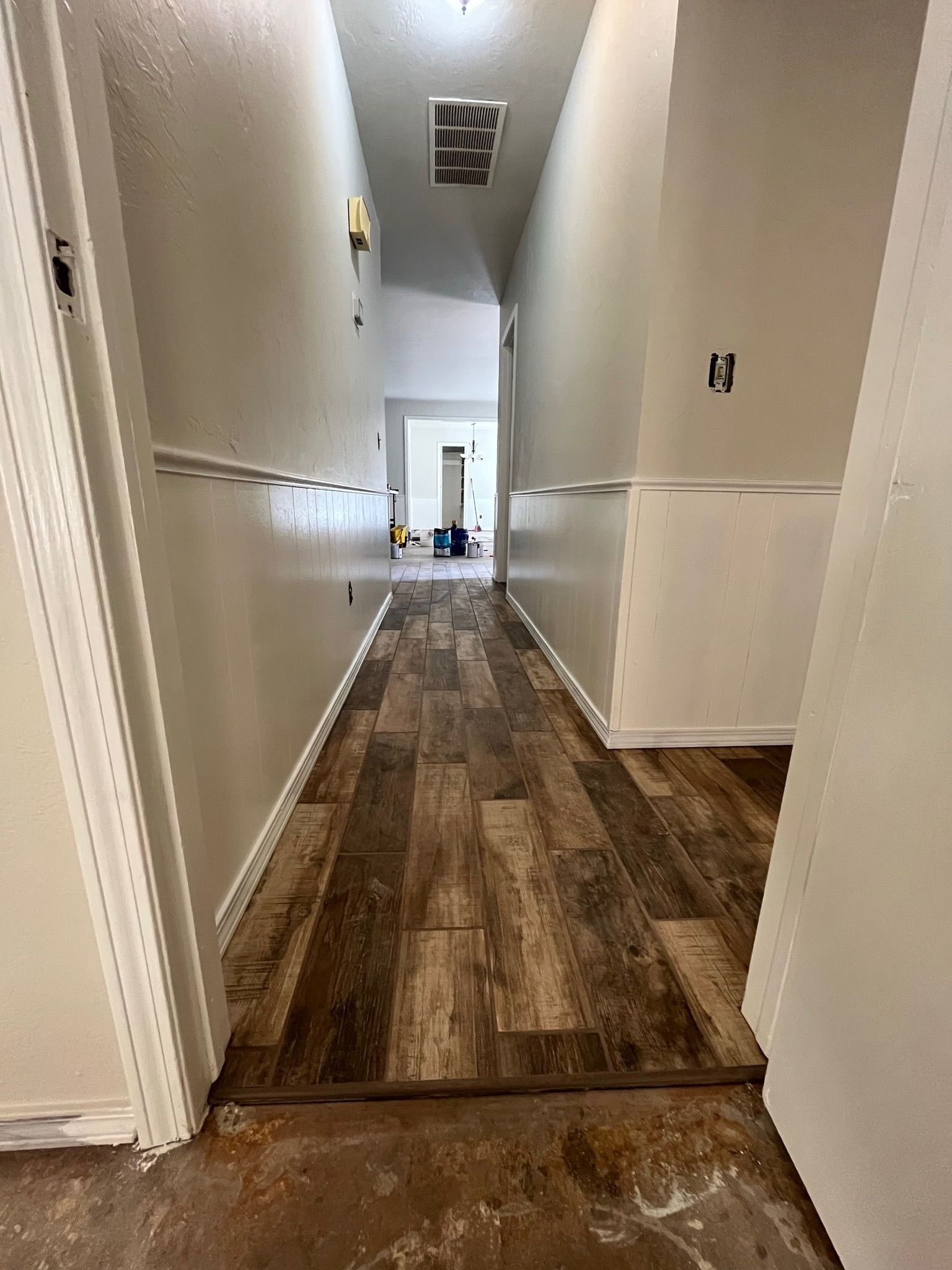 Hallway with wood-look flooring, white walls with wainscoting, unfinished electrical boxes.