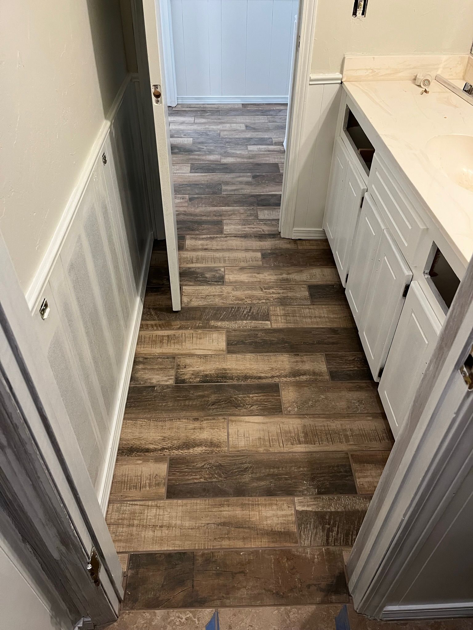 Narrow hallway with wood-look flooring. White cabinets on the right, and a white louvered panel on the left wall.