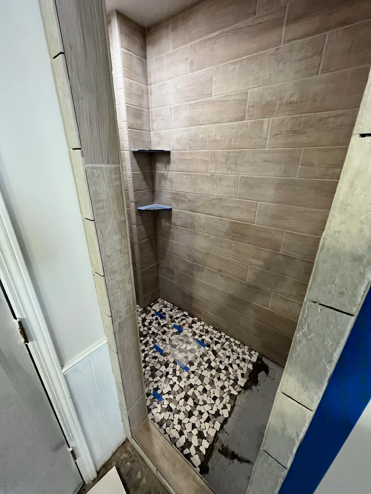 Shower with stone tile walls, pebble floor, and built-in shelves. Partially constructed, some areas covered.