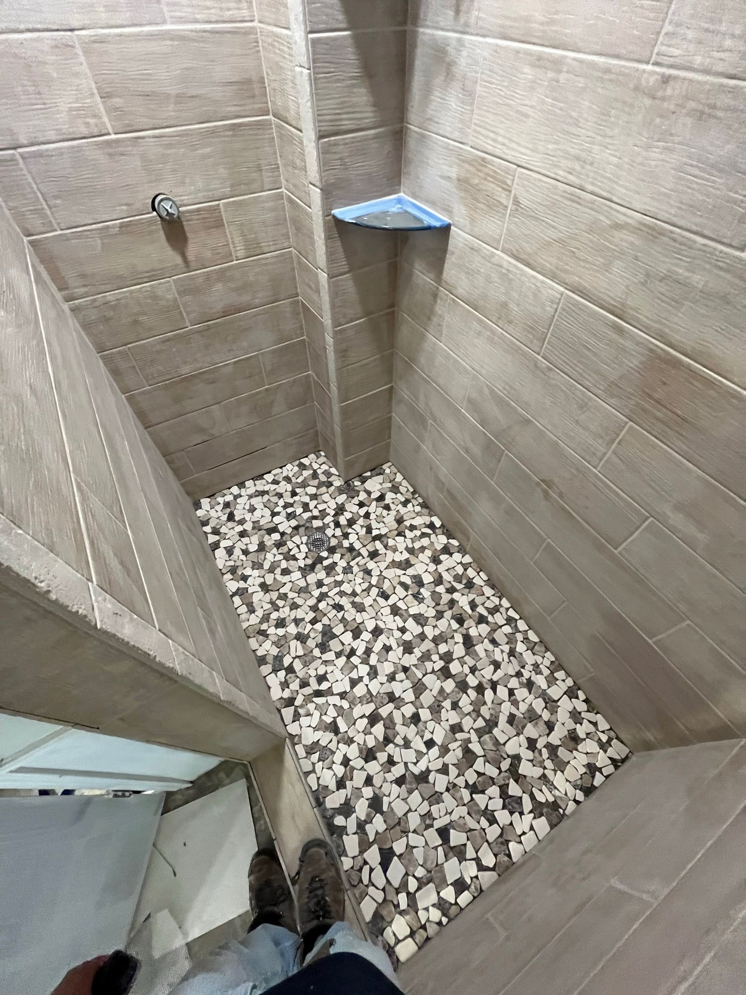 Shower with gray tile walls and a mosaic floor. A blue corner shelf is visible.