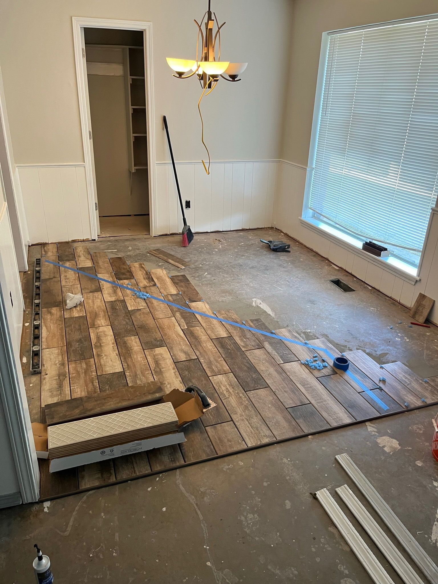 Room with wood-look flooring installation in progress. Brown, gray, and blue tones. A window and closet are visible.