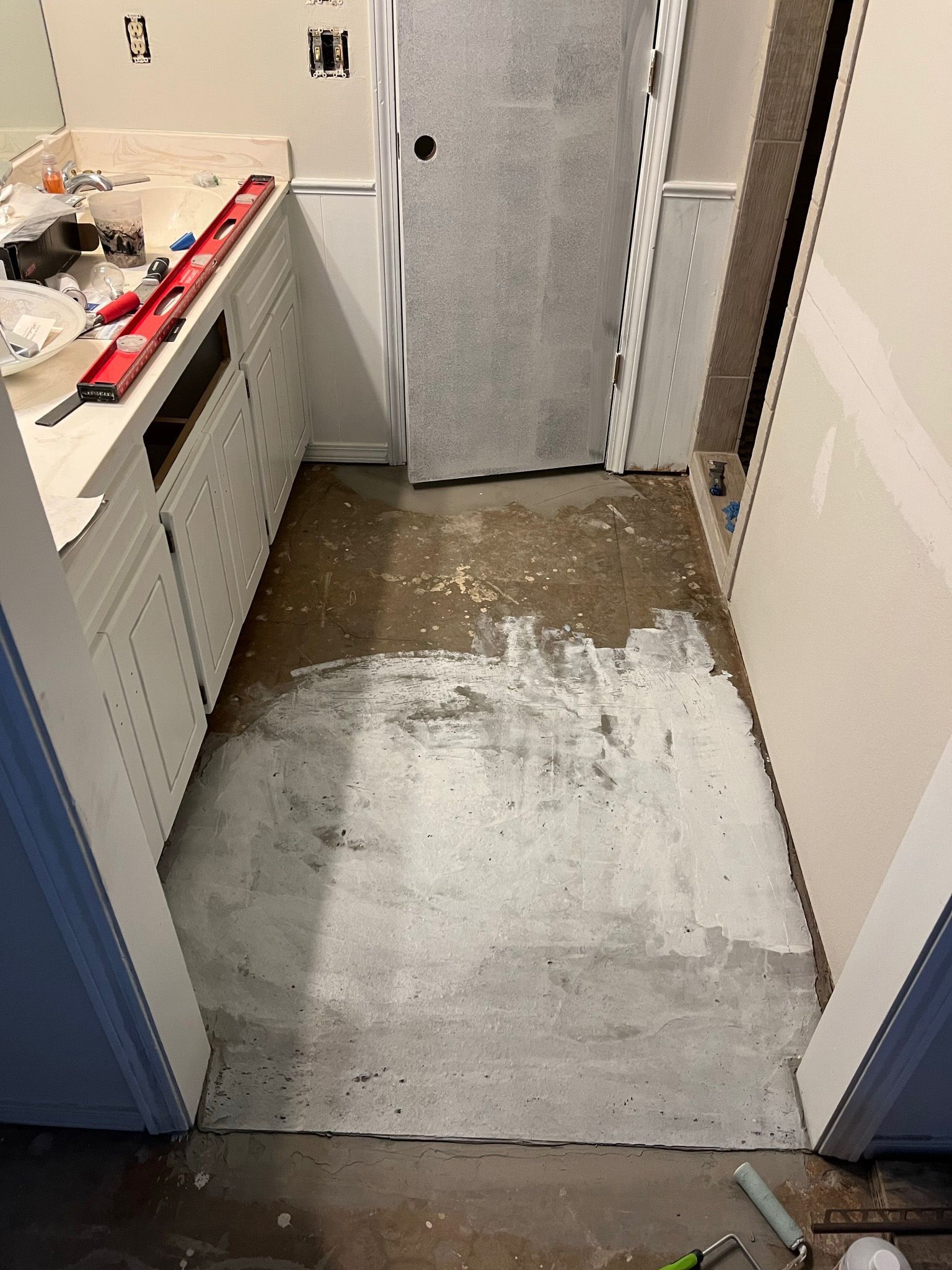 Bathroom under construction with a concrete floor, white cabinets, and a partially installed door.