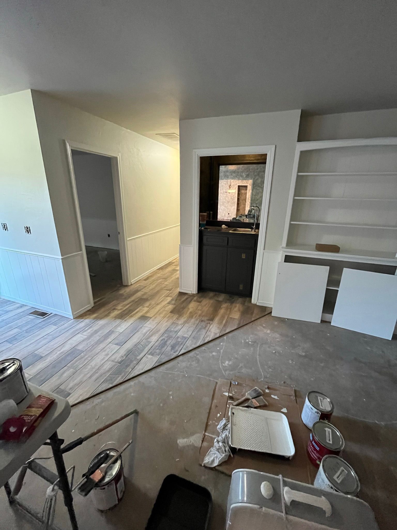 Interior room under renovation with paint cans, unfinished cabinets, and doorways.