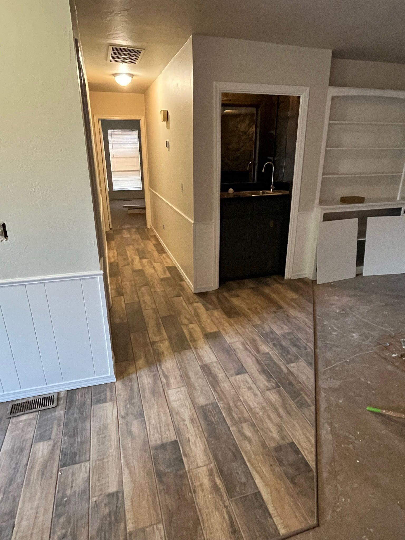 Interior view with wood-look flooring, hallway, open doorway to a dark sink area, and a built-in shelf.