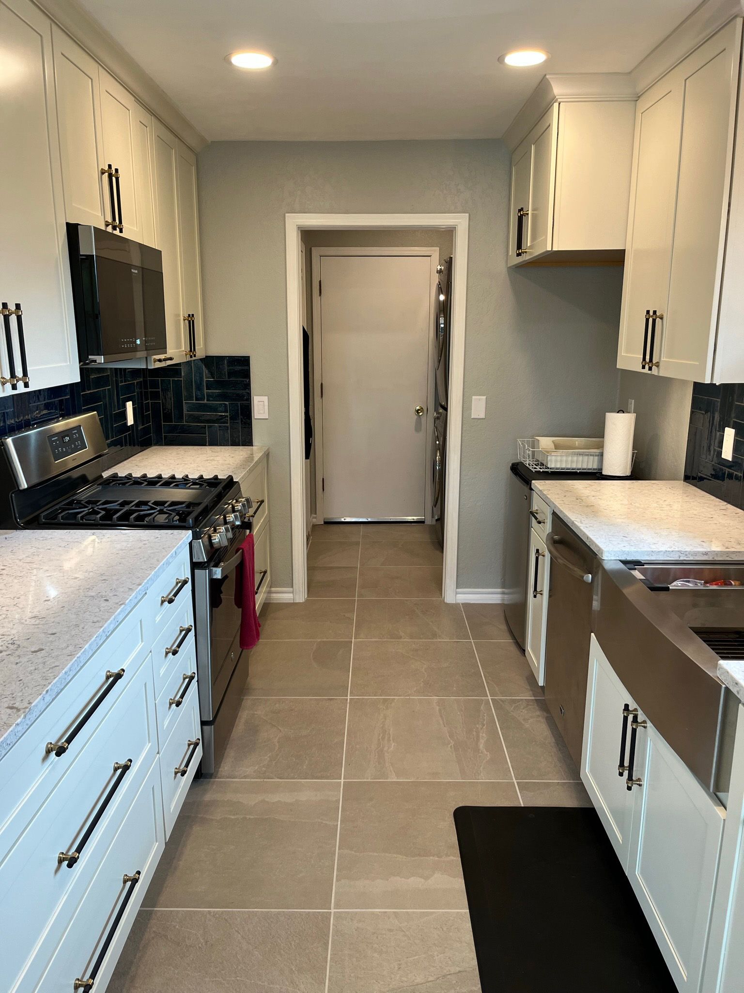 Narrow kitchen with white cabinets, stainless steel appliances, and beige tile floor.