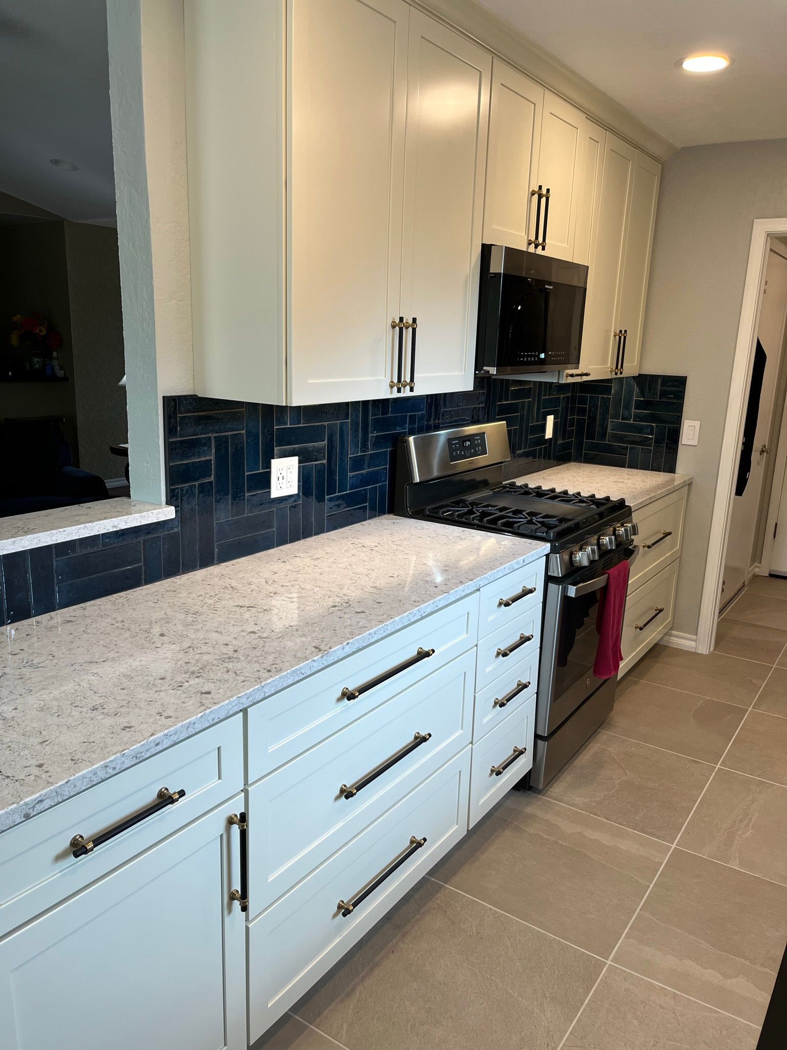 Light blue kitchen with white countertop, navy blue tile backsplash, and stainless steel appliances.