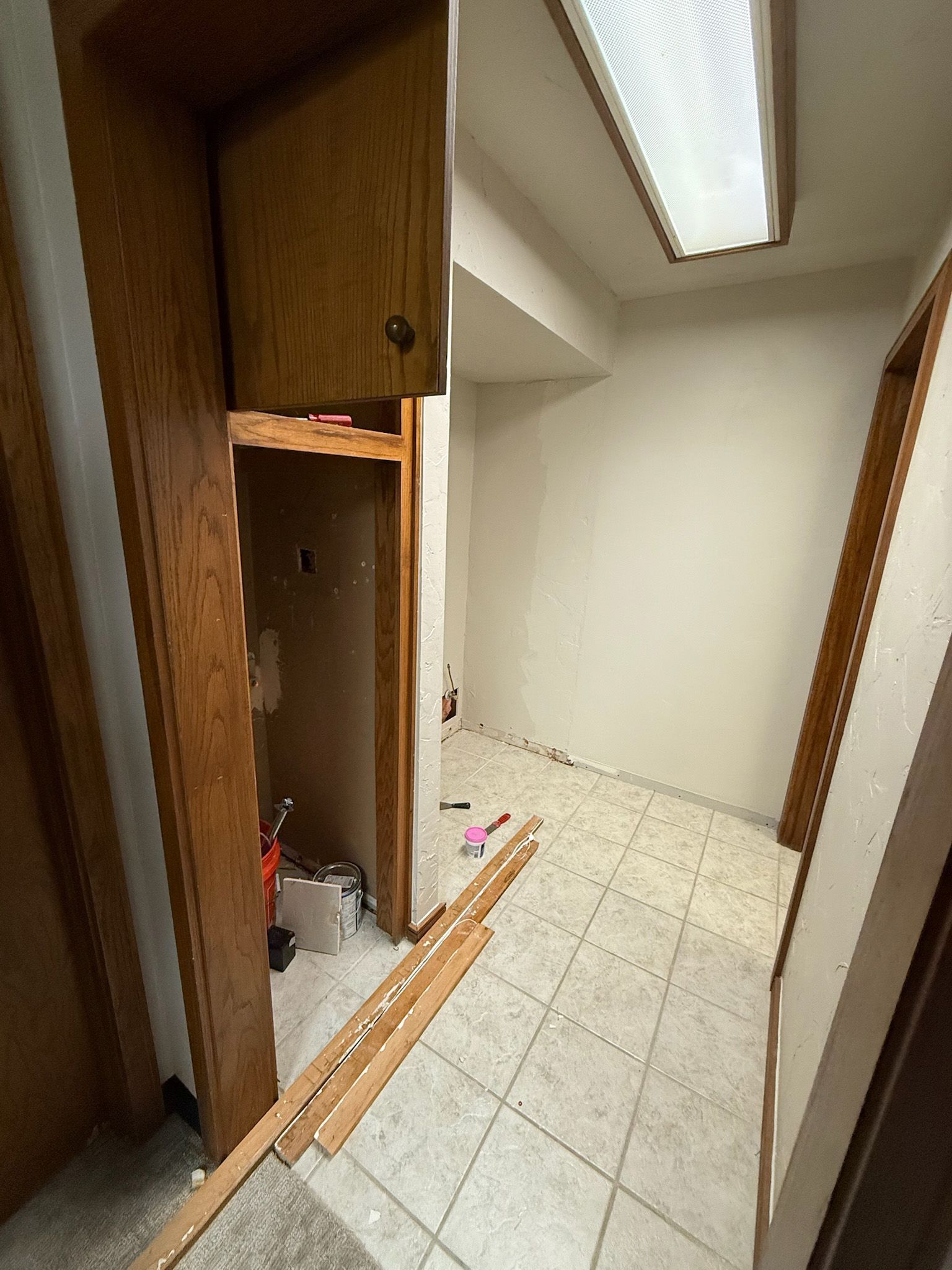 Hallway with partially removed cabinet, tools, and flooring; neutral walls and tile.