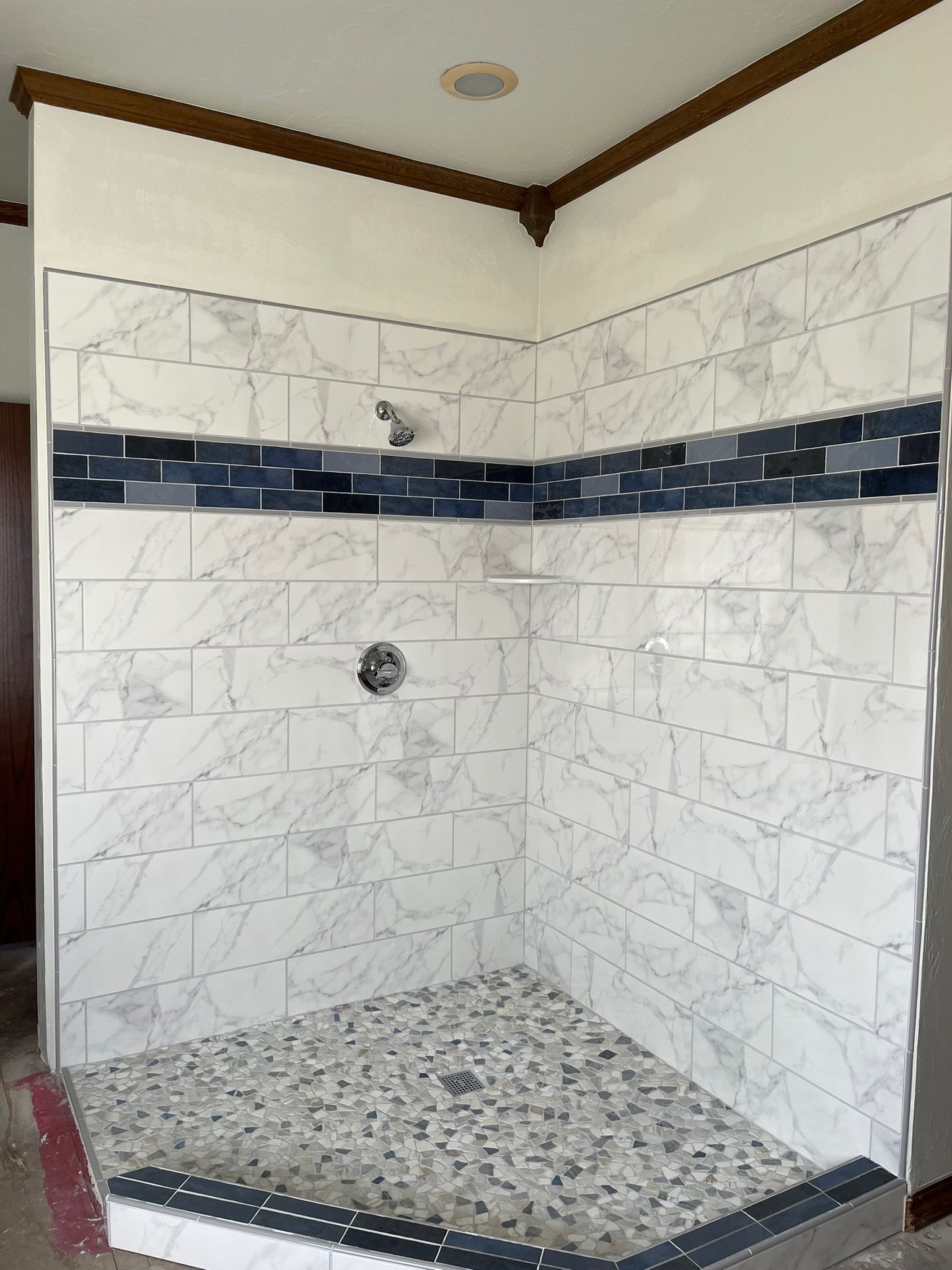 Tiled shower with white marble-look walls, a dark blue border, and pebble-tiled floor.