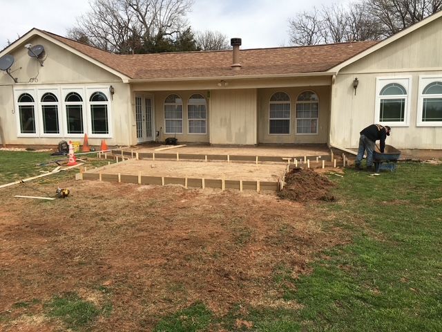 Backyard deck under construction; worker, framing, dirt, and grass.