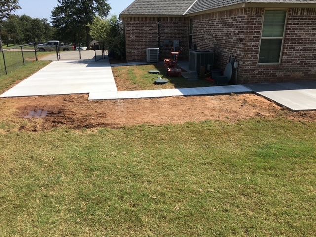Concrete walkways leading to a brick house on grass, with bare earth between them.