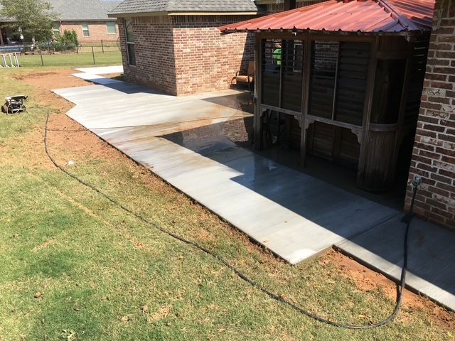 New concrete patio and walkway next to a brick house and a screened porch, on grass.