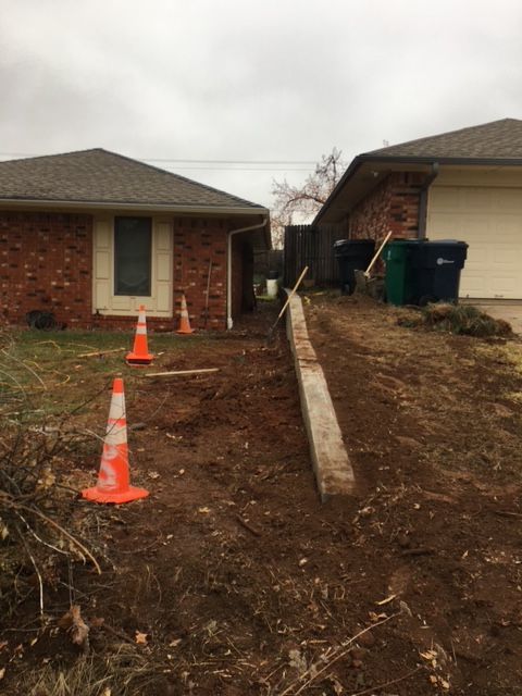 Dirt and construction debris between two brick houses. Orange traffic cones present. Overcast day.