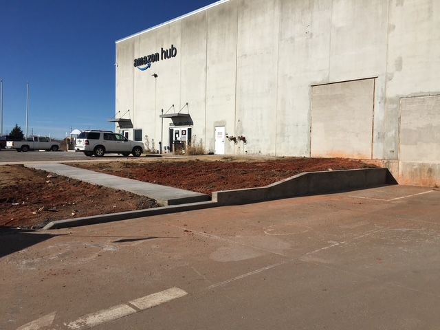 Amazon Hub building with a sidewalk, brown soil, and a white SUV on a clear day.