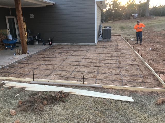 Concrete foundation being prepared for pouring in a yard. Man in orange shirt stands nearby.