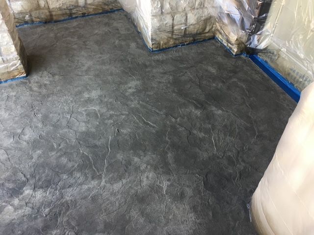Textured, gray concrete floor with blue tape along edges, next to stone walls.