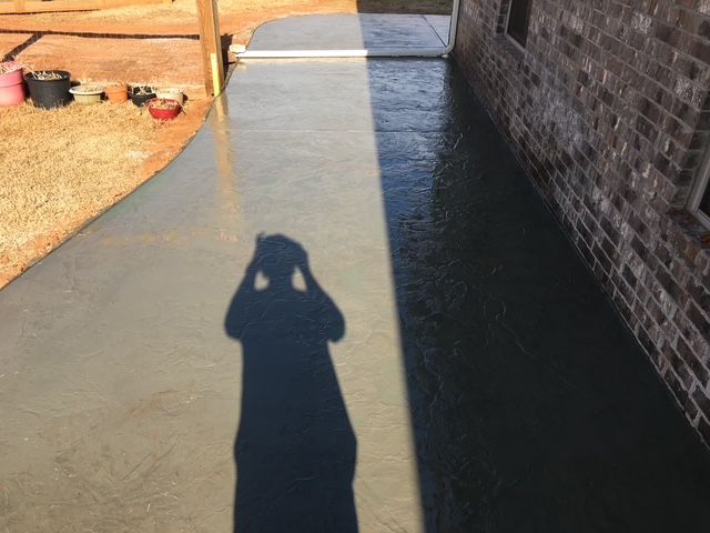 Shadow of a person on a wet, gray concrete patio beside a brick wall.