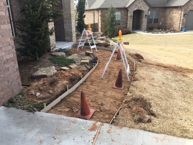 Pathway construction in front yard, orange cones and surveying equipment mark the path.