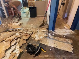 Man removing flooring in room, debris scattered. Blue painted columns and walls.