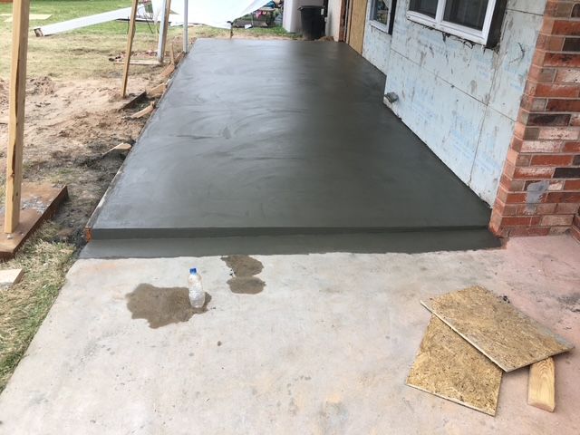 Freshly poured concrete porch with step next to a brick house, next to a gravel yard.