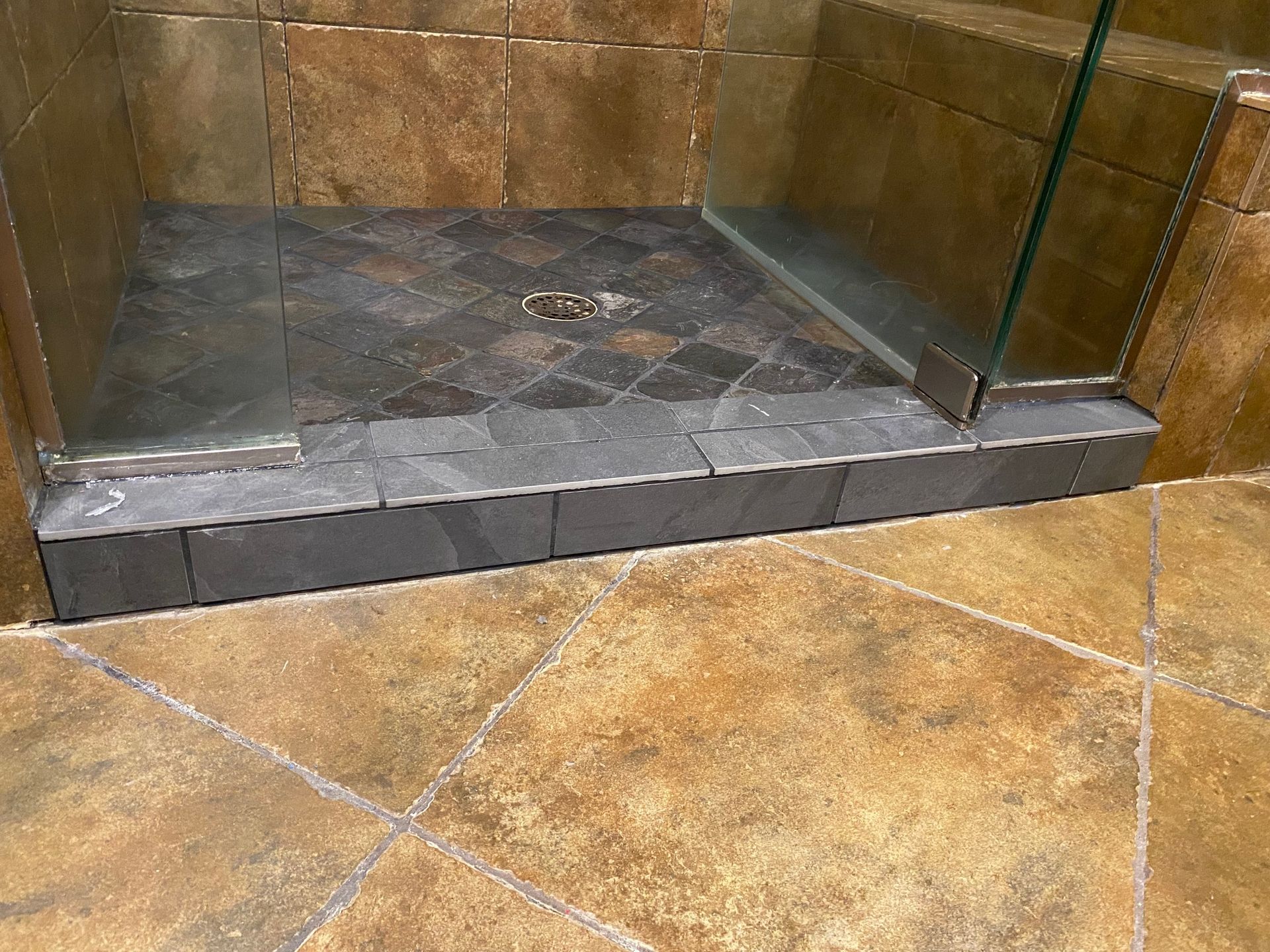 Shower with stone tile floor and a step over the edge to enter.