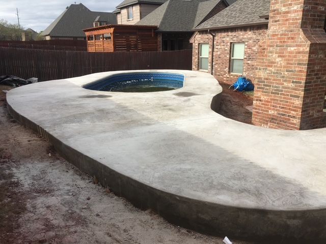Newly poured concrete pool deck surrounding a small, dark pool with brick chimney.