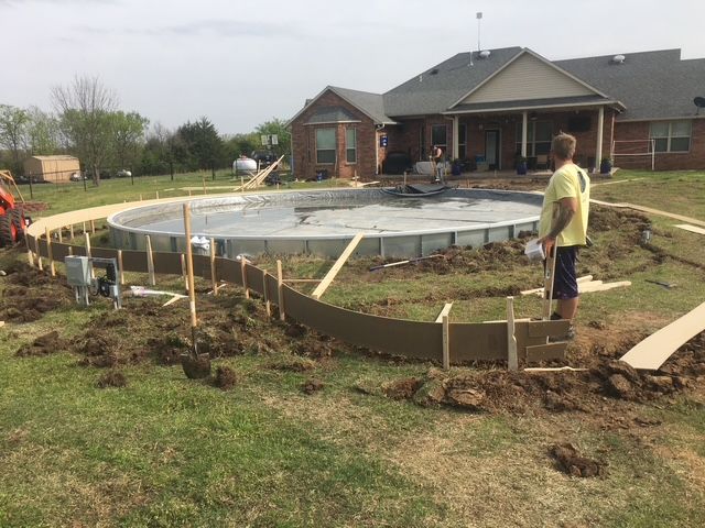 Construction site with workers building a round pool. A house is in the background.