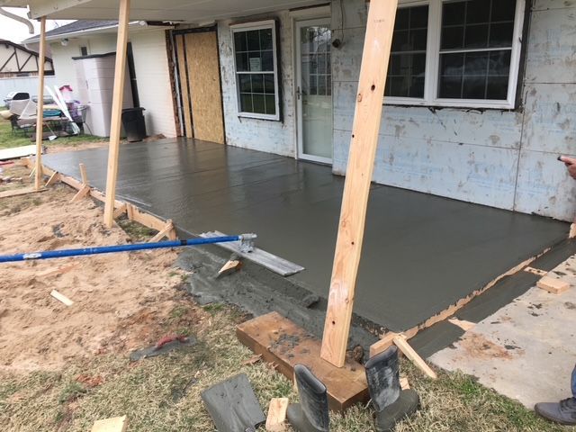 Newly poured concrete patio being leveled, next to a house, outdoors.