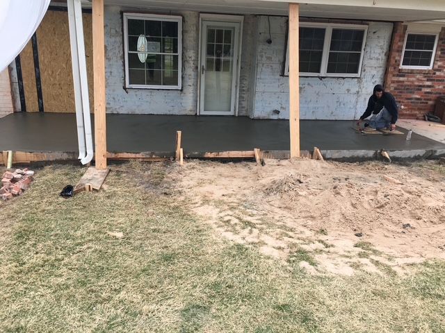 Newly poured concrete porch; worker smoothing surface, set in front of house.