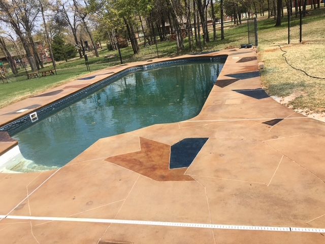 Outdoor rectangular pool with brown concrete decking. Dark water, trees in background.