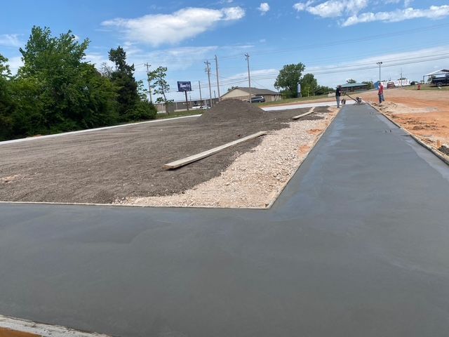 Newly poured concrete sidewalk and parking area under construction outdoors on a sunny day.