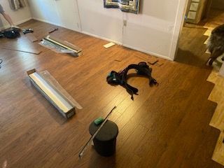 Wood-look flooring installation in progress. Boxes, tools, and a dark object are on the floor.