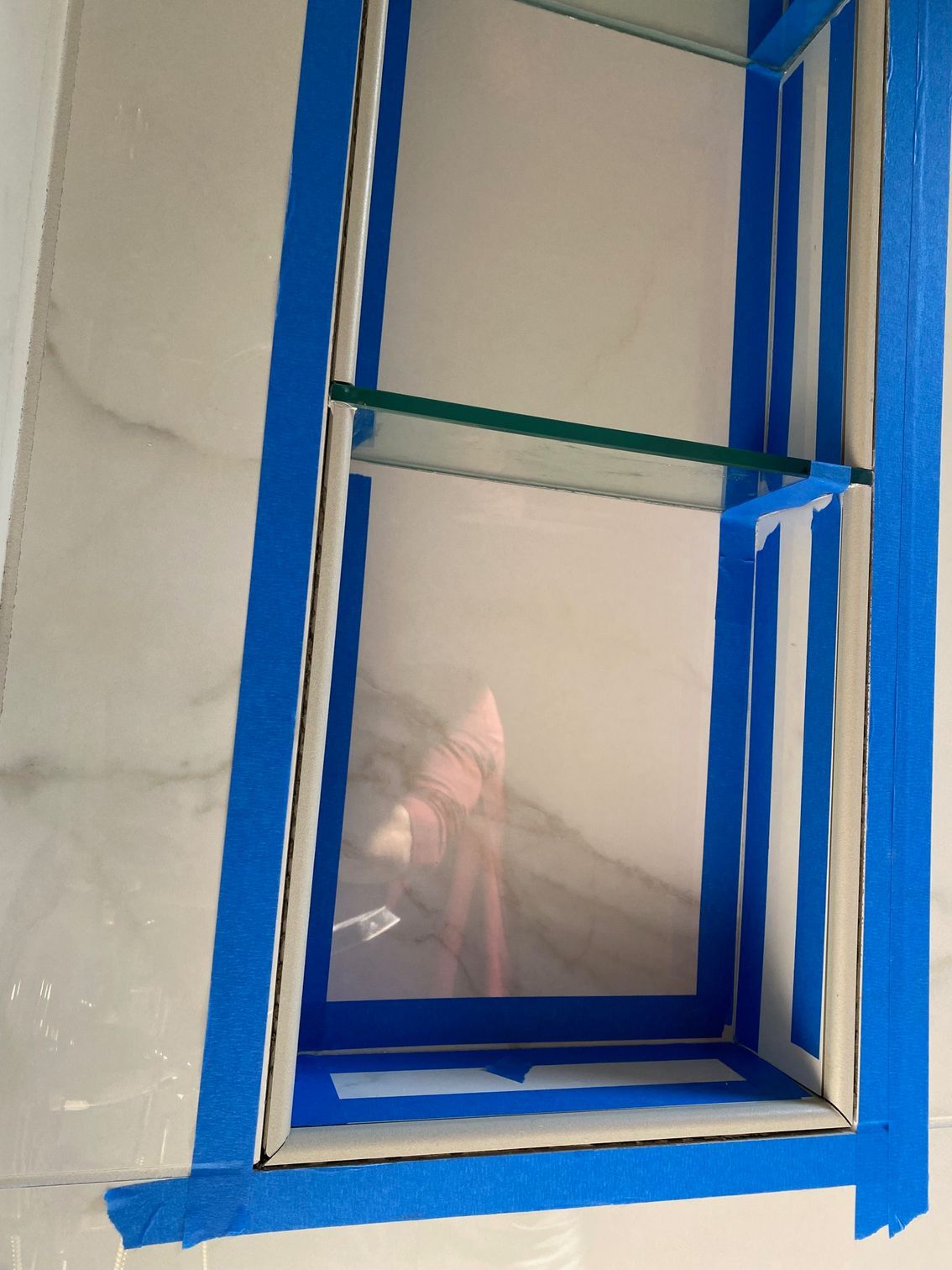 A recessed bathroom shelf taped for sealing; glass shelves and white tile.