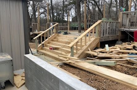 Wooden deck and stairs under construction. Lumber, tools, and debris scattered around.