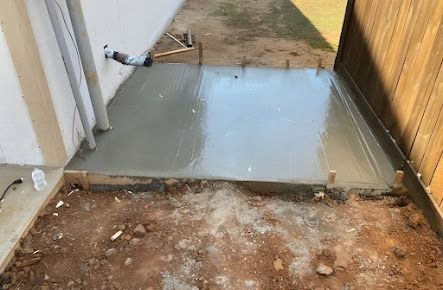Freshly poured concrete patio with wooden borders next to a fence and wall.