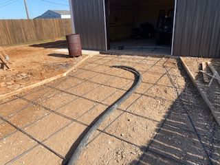 Concrete slab construction, rebar grid, black hose, shed entrance, outdoor setting.