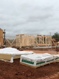 Construction site with wooden frame of a building, stacks of materials on the ground, cloudy sky.