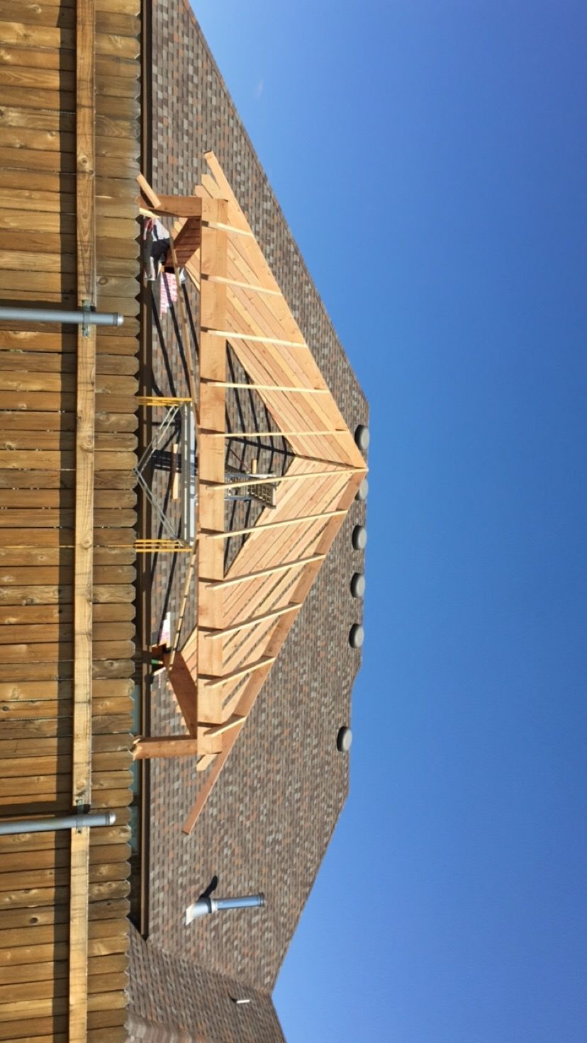 Construction worker on a roof installing wooden frame against a blue sky.