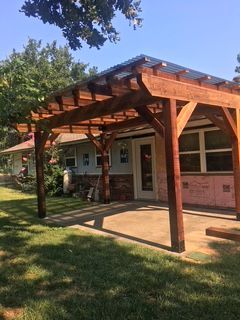 Wooden pergola over a concrete patio attached to a house with a grassy lawn.