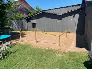 A backyard with a dirt area roped off with caution tape, next to a gray building.